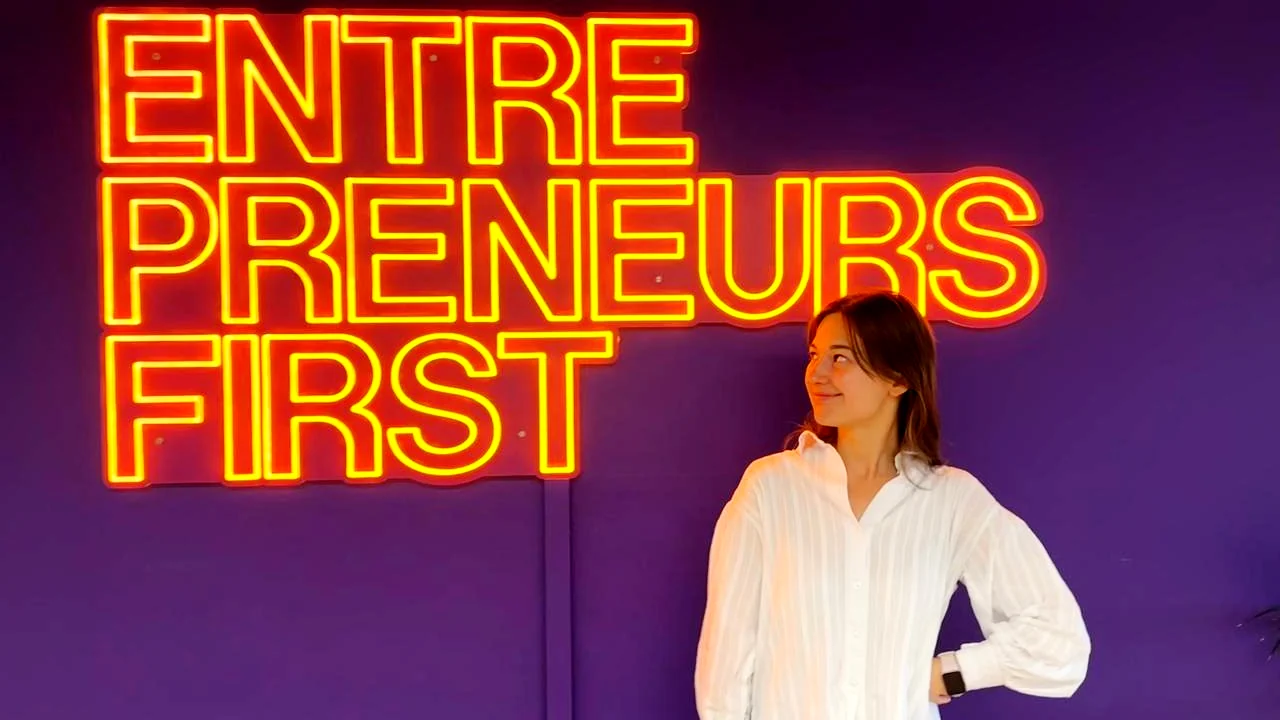 Alina at the Entrepreneurs First office, under the neon EF sign